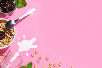 Pink breakfast background with cereal rings, cherries, mint leaves, a spoon, spilled milk, and a bowl. Space for your text.