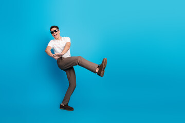 Cheerful man in sunglass posing against a vibrant blue background in casual attire, expressing...