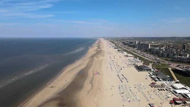 Aerial view of the sandy beach meeting the blue sea, dotted with colorful umbrellas and beachgoers enjoying a sunny day, Zandvoort, North Holland, Netherlands.