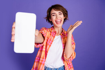 Portrait of nice young lady show empty space smart phone display wear shirt isolated on purple...