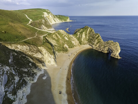 Aerial view of Durdle Door's majestic arch meets the turquoise sea, cradling a sandy beach beneath chalky cliffs in soft light, Wareham, Dorset, United Kingdom.