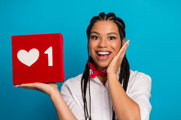 Joyful young woman holding a red box with a heart icon symbolizing likes against a blue background