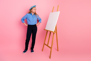 Young artist in casual outfit stands by blank canvas on easel, cheerful creative expression against...