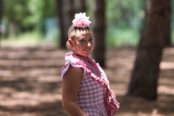 A beautiful young Spanish woman dressed in a traditional pink and white flamenco dress with a...