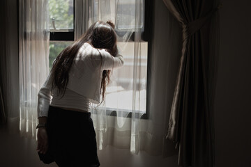 Sad and depressed young asian woman standing at window in the bedroom, Woman worry, Unhappy girl.