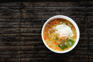 Rice porridge or boiled rice soup and seasoned minced pork with soft -boiled egg in whiite bowl on bamboo table background.Top view.