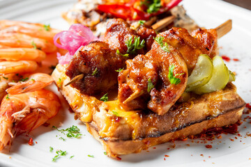 Grilled chicken skewers and cooked shrimp served on a waffle, garnished with fresh parsley on a...