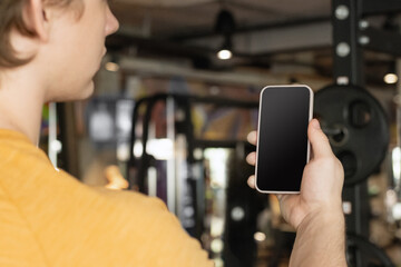 Athlete standing and displaying smartphone with white blank screen in gym setting. Mock up. Space...