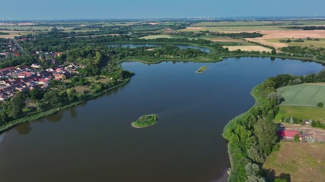 Aerial view of a serene lake mirroring the clear sky, bordered by lush greenery and the quaint town of Penkun, Uckermark, Brandenburg, Germany.