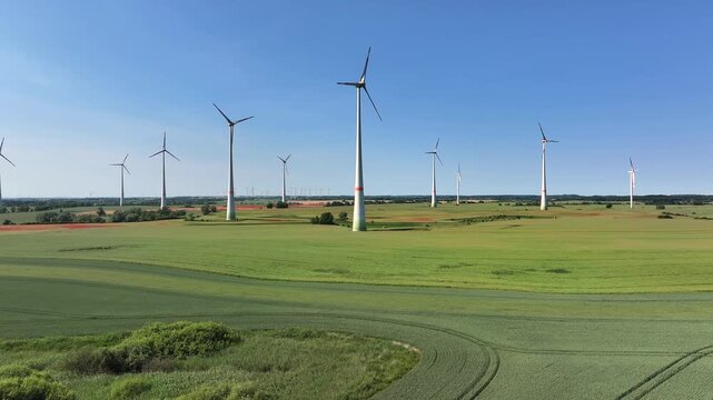 Aerial view of multiple wind turbines standing tall within a vast green field under a clear blue sky, showcasing renewable energy, Brussow Uckermark, Brandenburg, Germany.