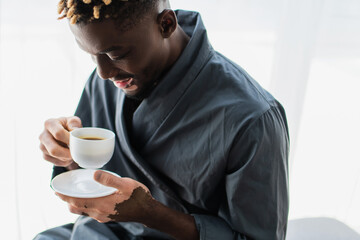 Carefree african american man with vitiligo holding cup of coffee at home