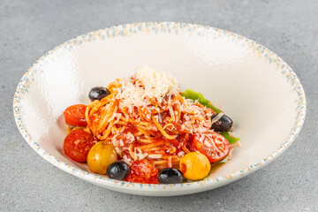 A vibrant plate of spaghetti with tomato sauce is topped with grated cheese, cherry tomatoes, black olives, and yellow cherry peppers