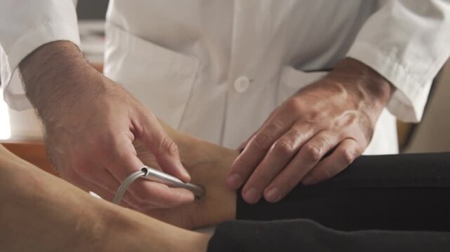 Close-up of an angiologist performing a laser Doppler test. The doctor switches the device between hands and places it on different areas of the patient&rsquo;s foot.