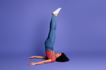 Young woman in casual outfit performing yoga posture on purple background embodying balance,...