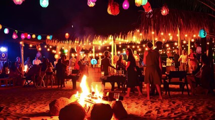 Vibrant beach gathering at night featuring lanterns, a bonfire, and a lively atmosphere with friends enjoying the scene