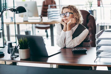 Young professional woman at her workspace reflecting on ideas while sitting at an elegant desk with...