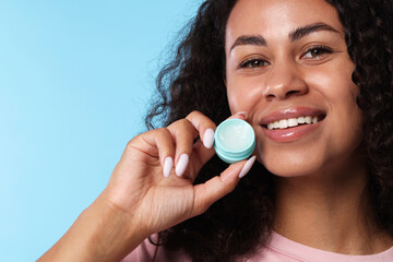 Smiling woman with lip balm on light blue background