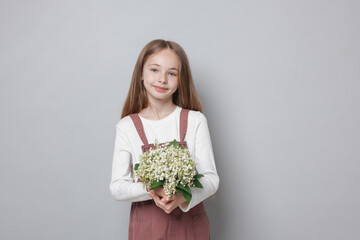 Girl with bouquet of beautiful lily-of-the-valley flowers on light grey background