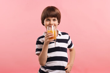 Cute little boy drinking orange juice on pink background. Refreshing drink