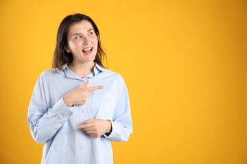 Surprised woman pointing at something on orange background, space for text