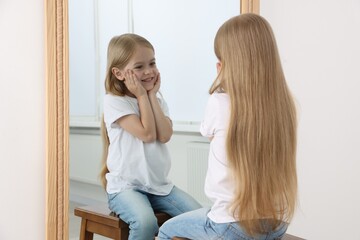 Beautiful little girl looking at herself in mirror indoors