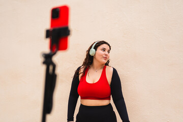 Curvy fitness influencer recording online workout content using smartphone and headphones