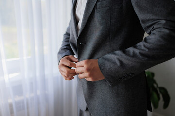 Man adjusting gray suit jacket in indoor setting near window during daytime