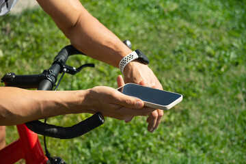 Cyclist standing and checking fitness progress in apps after riding with smartphone. Summer...