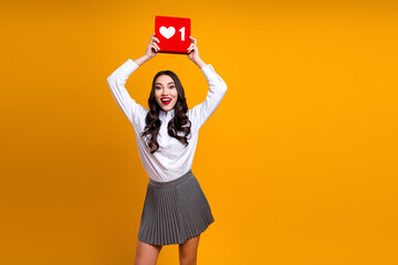 Young stylish woman happily holding like sign gesture symbolizing social media likes on vibrant yellow background