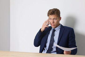 Young businessman with papers complaining to someone via phone at wooden table indoors, space for...