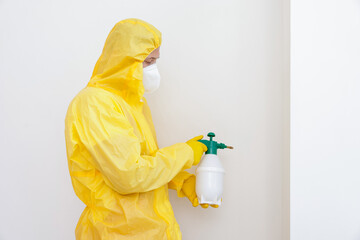 Pest control worker in protective suit spraying insecticide near white wall. Space for text