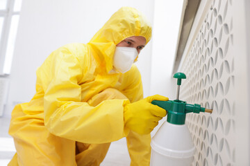 Pest control worker in protective suit spraying insecticide indoors, selective focus