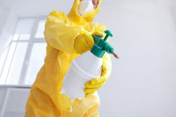 Pest control worker in protective suit spraying insecticide indoors, closeup