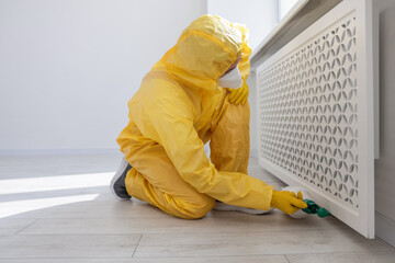 Pest control worker in protective suit spraying insecticide indoors