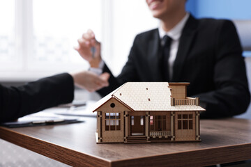 Real estate agent giving key to client at desk in office, focus on house model