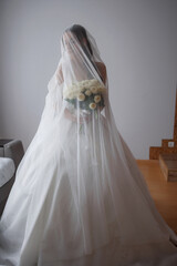 Elegant bride holding bouquet while preparing for wedding ceremony indoors