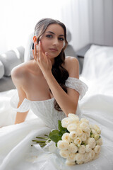 Elegant bride posing with bouquet in soft, romantic setting before wedding ceremony