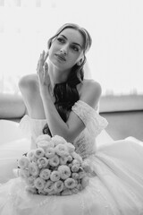Bride in elegant gown poses with bouquet, capturing a moment of reflection in soft light