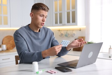 Sick man with pills having online consultation with doctor via laptop at white marble table in...