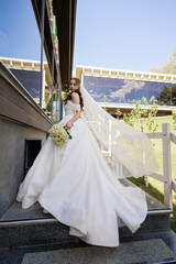 Bride in elegant white dress descends stairs at outdoor venue on sunny day