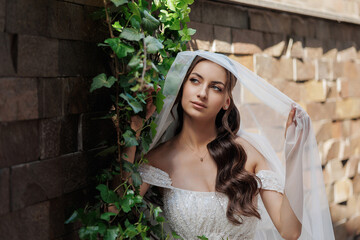 Bride with elegant veil surrounded by greenery in a serene outdoor setting