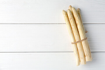 Bunch of raw asparagus spears on white wooden table, top view. Space for text