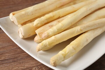 Raw white asparagus spears on wooden table, closeup