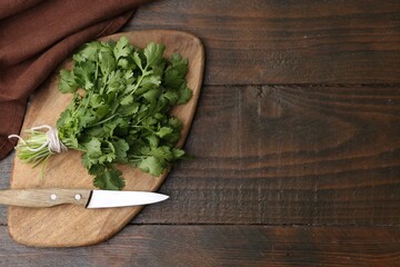 Cutting board with fresh cilantro and knife on wooden table, top view. Space for text