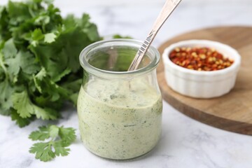 Tasty cilantro sauce and spoon in jar on light marble table, closeup