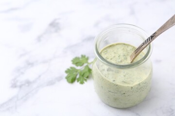 Tasty cilantro sauce and spoon in jar on light marble table, closeup. Space for text