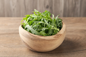 Fresh ripe green arugula leaves in bowl on wooden table, closeup
