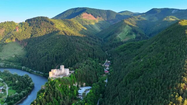 Tatra mountains covered with lush green pine tree forests in Slovakia. Drone footage approaching the Strecno Castle on the rock over the river.