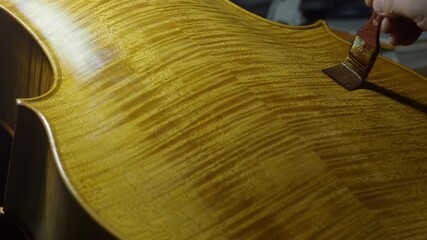 Skilled luthier brushing varnish onto cello back plate marbling, preserving traditional craftsmanship in wooden workshop setting, slow motion - Powered by Adobe