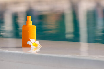 Close-up of a sunscreen spray bottle mockup with a tropical flower nearby. Concept summer skincare...